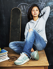 Image showing young cute teenage girl in classroom at blackboard seating on ta