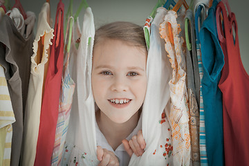 Image showing portrait of a little girl standing near a hanger with clothes