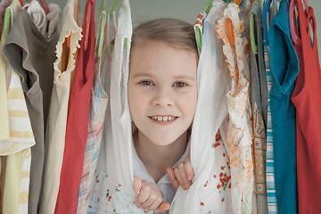 Image showing portrait of a little girl standing near a hanger with clothes