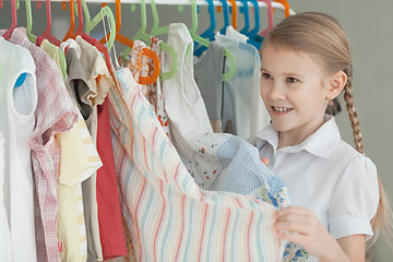 Image showing portrait of a little girl standing near a hanger with clothes