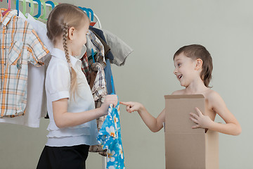 Image showing Two little children standing near a hanger with clothes at home 