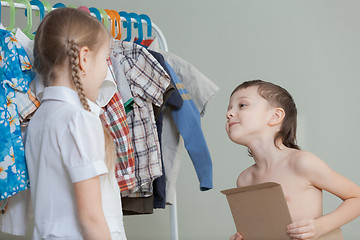 Image showing Two little children standing near a hanger with clothes at home 