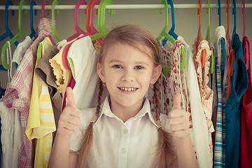 Image showing portrait of a little girl standing near a hanger with clothes