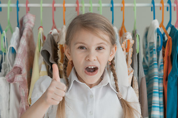 Image showing portrait of a little girl standing near a hanger with clothes