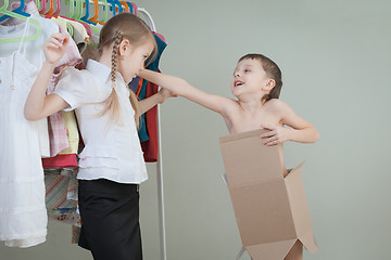 Image showing Two little children standing near a hanger with clothes at home 