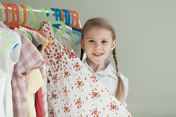 Image showing portrait of a little girl standing near a hanger with clothes