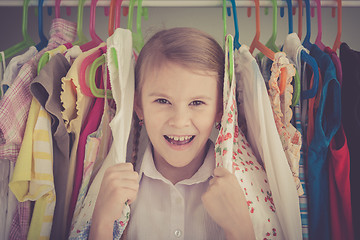 Image showing portrait of a little girl standing near a hanger with clothes