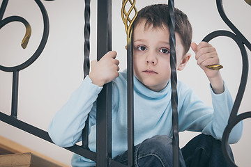 Image showing one sad little boy sitting on the stairs in house at the day tim