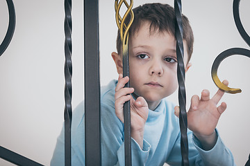 Image showing one sad little boy sitting on the stairs in house at the day tim