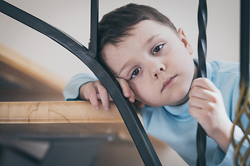 Image showing one sad little boy sitting on the stairs in house at the day tim