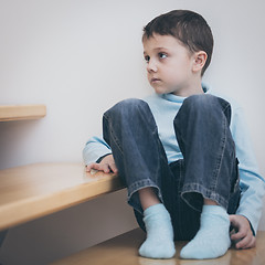 Image showing one sad little boy sitting on the stairs in house at the day tim