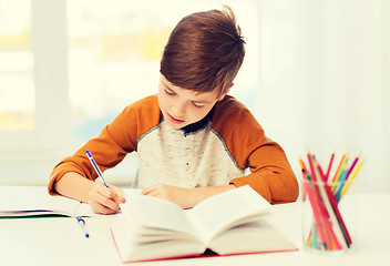 Image showing student boy with book writing to notebook at home