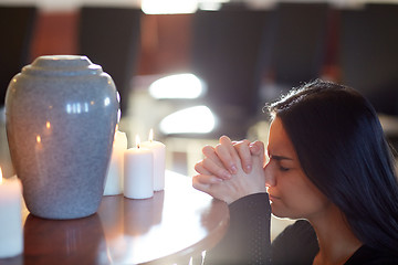 Image showing sad woman with funerary urn praying at church