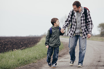 Image showing Father and son walking on the road at the day time. 