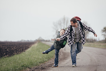 Image showing Father and son walking on the road at the day time.