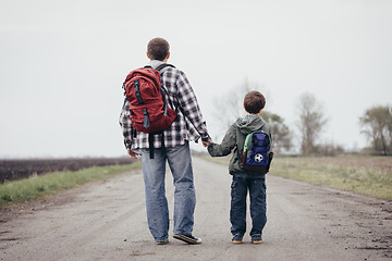 Image showing Father and son walking on the road at the day time.