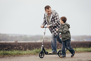 Image showing Father and son walking on the road at the day time.