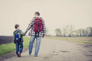 Image showing Father and son walking on the road at the day time.