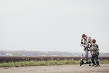 Image showing Father and son walking on the road at the day time.