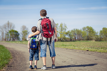 Image showing Father and son walking on the road at the day time.