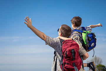 Image showing Father and son walking on the road at the day time.