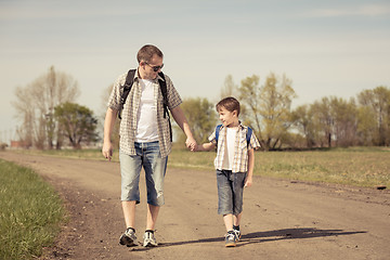 Image showing Father and son walking on the road at the day time.