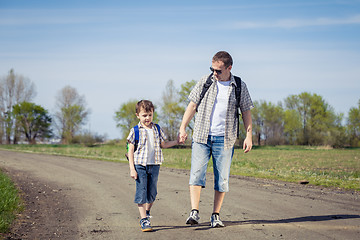 Image showing Father and son walking on the road at the day time. 