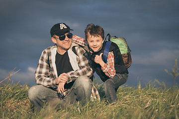 Image showing Father and son walking on the road at the day time.