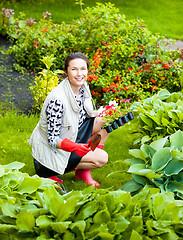 Image showing Beautiful smiling woman planting flowers in a flower garden