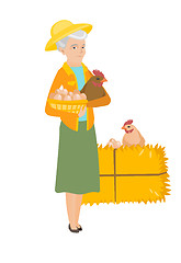 Image showing Senior farmer holding chicken and basket of eggs.