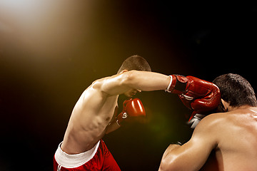 Image showing Two professional boxer boxing on black background,