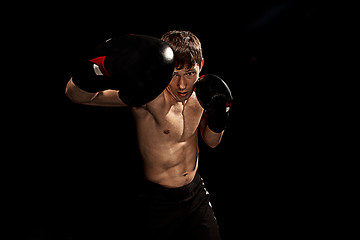 Image showing Male boxer boxing in punching bag with dramatic edgy lighting in a dark studio