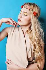 Image showing young pretty blond girl with curly blond hair and little lowers happy smiling on blue sky background, lifestyle people concept