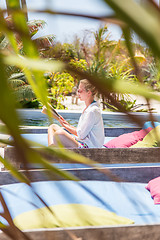 Image showing Candid shot of lady reading book and relaxing in lush tropical garden.