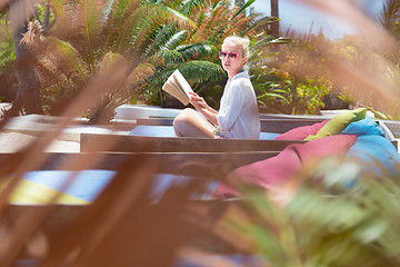 Image showing Candid shot of lady reading book and relaxing in lush tropical garden.