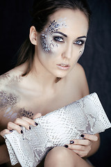 Image showing fashion portrait of pretty young woman with creative make up like a snake, fashion victim with python skin clutch luxury