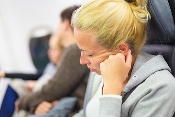 Image showing Tired blonde woman napping on seat while traveling by airplane.