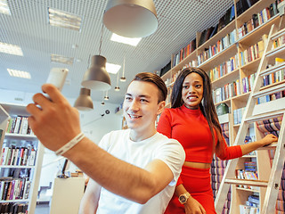 Image showing couple students in univercity library, looking book, preparing to exam, having fun, making selfie, lifestyle people concept