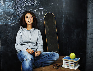 Image showing young cute teenage girl in classroom at blackboard seating on table smiling, modern hipster concept, lifestyle people