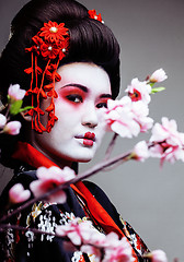 Image showing young pretty geisha in kimono with sakura and red decoration design on white background