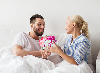 Image showing happy couple with gift box in bed at home