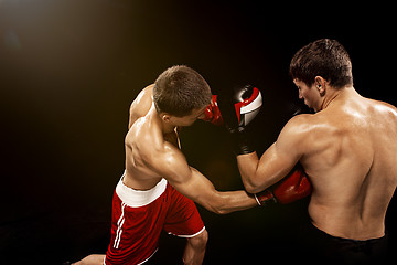 Image showing Two professional boxer boxing on black background,