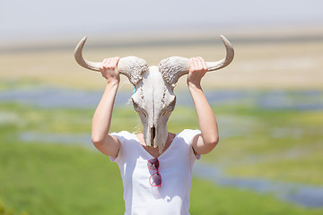 Image showing Woman holding a white wildebeest skull wearing it like a mask in nature on african wildlife safari.