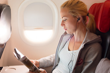Image showing Woman reading magazine and listening to music on airplane.