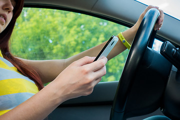 Image showing Woman driver sitting behind the steering wheel reading a text message on a mobile