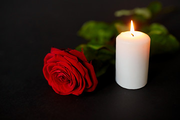 Image showing red rose and burning candle over black background