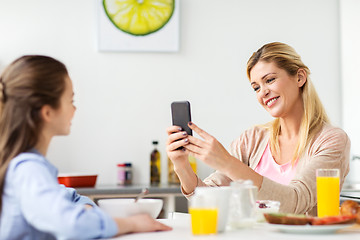 Image showing woman photographing daughter by smartphone at home