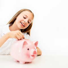 Image showing happy smiling girl putting coin into piggy bank