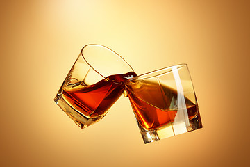 Image showing Two whiskey glasses clinking together on brown