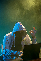 Image showing Hooded computer hacker stealing information with laptop